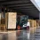 A forklift transporting a stack of wooden pallets in the loading area of ​​an industrial warehouse, featuring multiple pallet stacks and a floor wet from the rain.